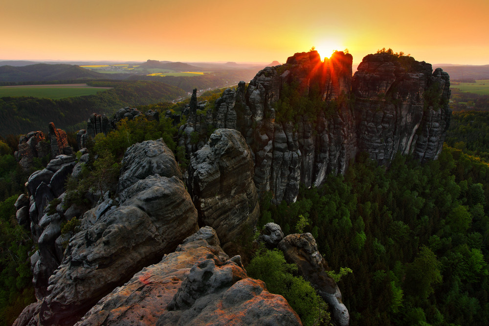 Schrammsteine, beautiful evening view over sandstone cliff into deep misty valley in Saxony Switzerland, foggy background, the fog is orange due to sunset, star sun on sky, Germany