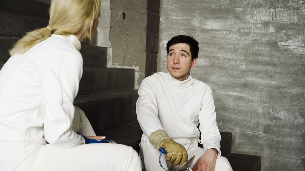 Two fencers man and woman sharing experience during break of fencing match indoors