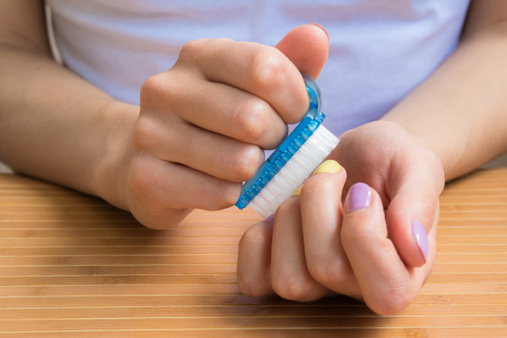 Female hands holding a nail brush. A young girl sits at a table and prepares manicure nail brush closeup.