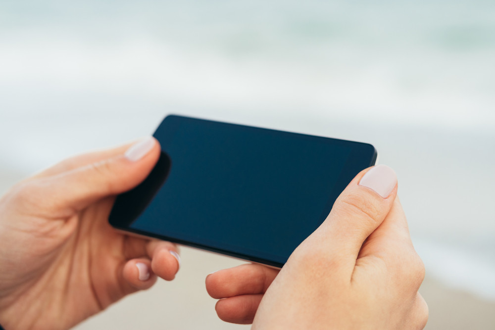 Female hands holding phone with touch screen on the background of the sea. Shallow depth of field.