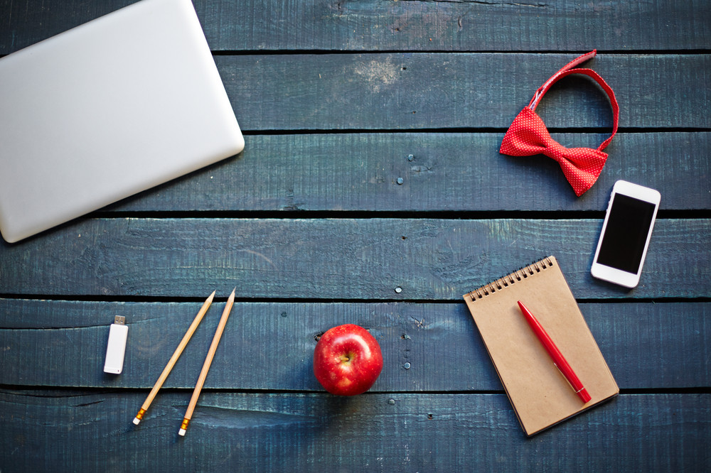 Technological devices, bowtie, red apple, pencils and notebook with pen on workplace