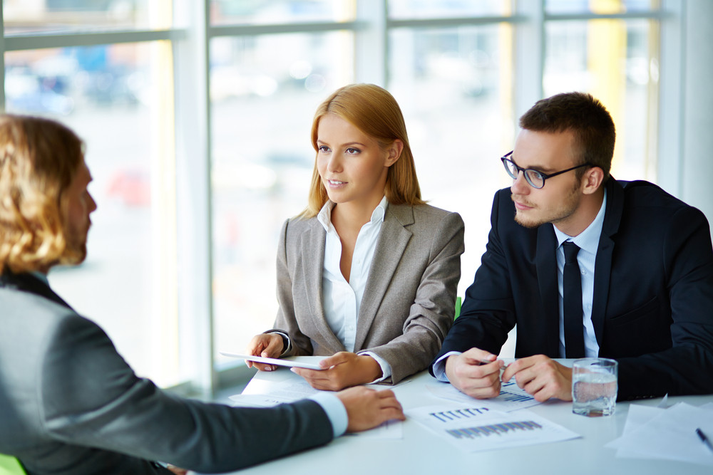 Two serious business partners listening attentively to young man at ...