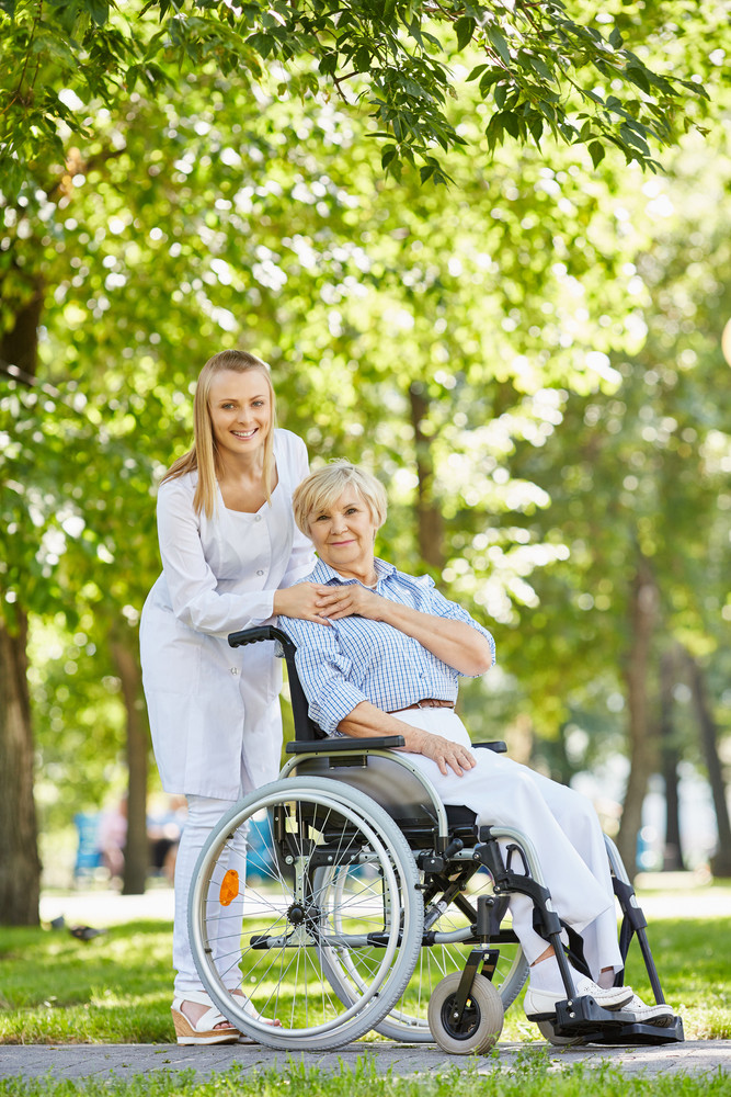 Young nurse and senior patient in a wheelchair looking at camera in park