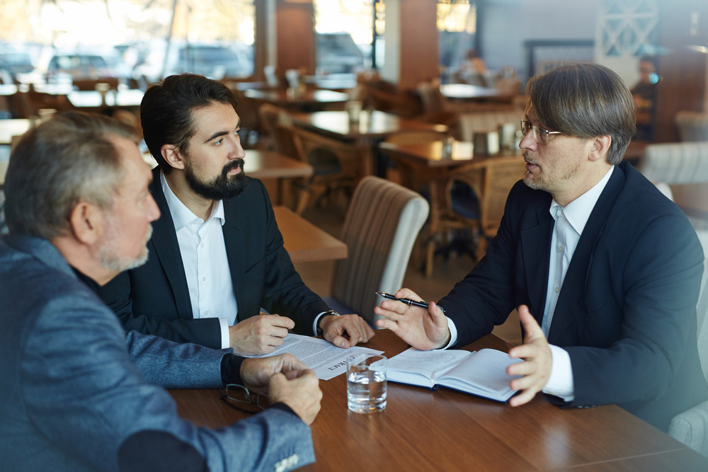 Business partners discussing terms and conditions before signing contract while having formal meeting in spacious restaurant, waist-up portrait