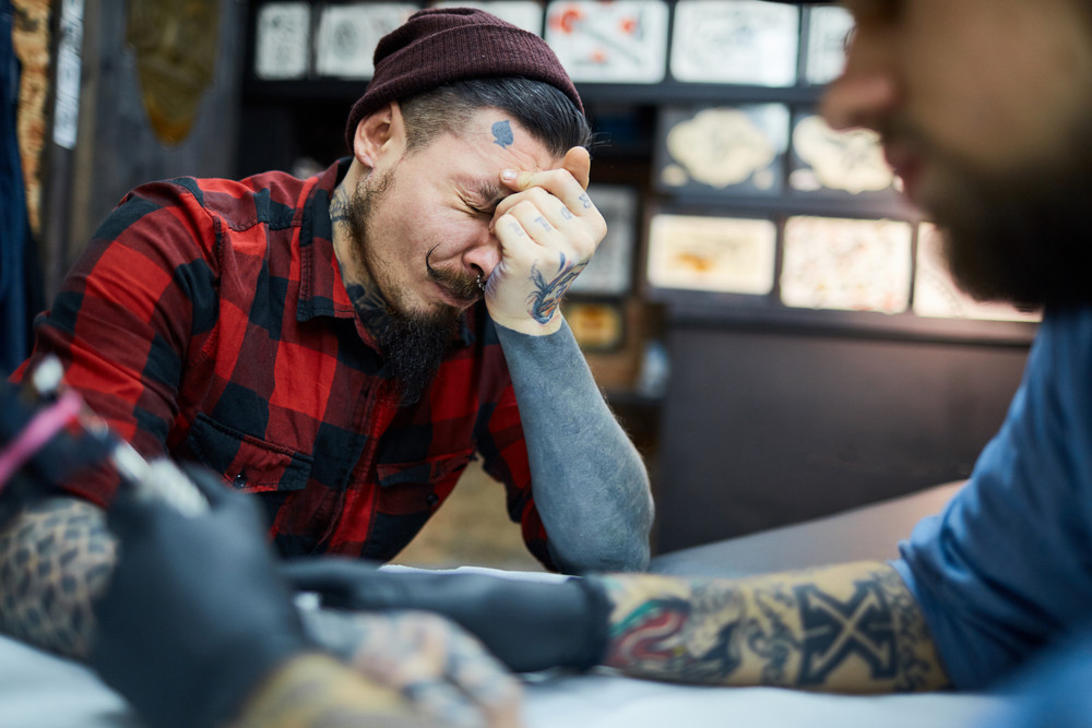 Client of tattoo salon feeling pain during process of tattooing
