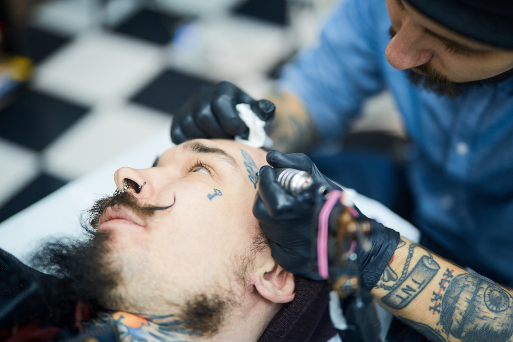 Master of tattoo art drawing on man face