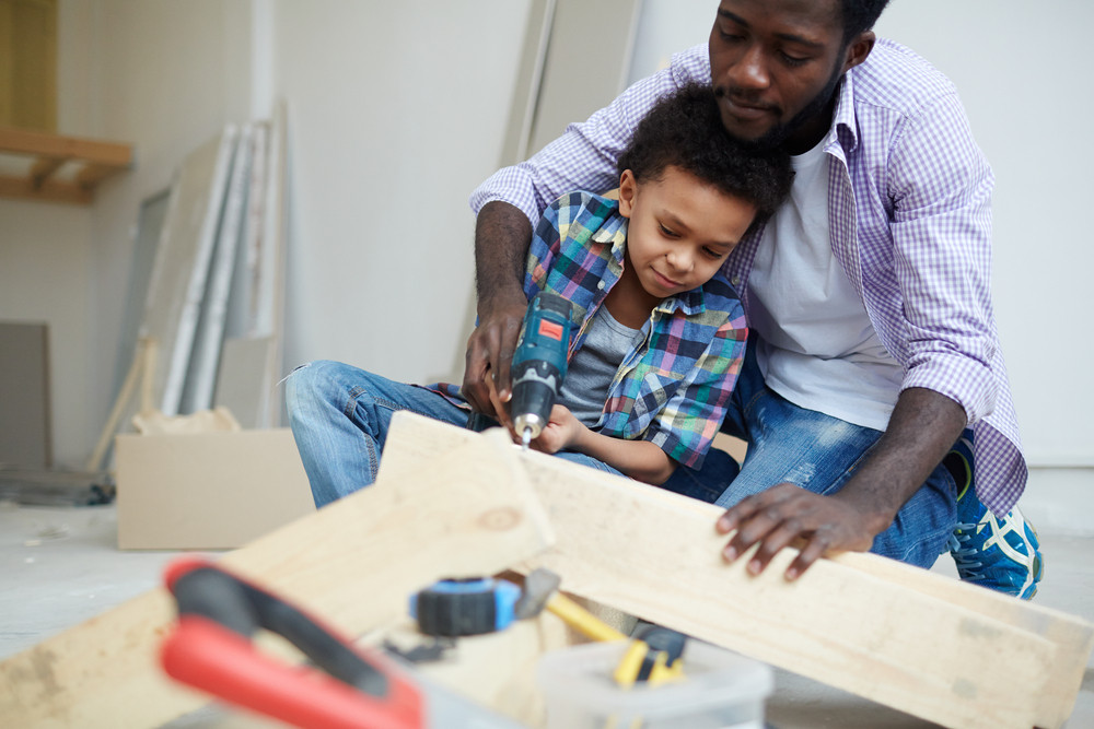 Young man showing his son how to work with electric drill