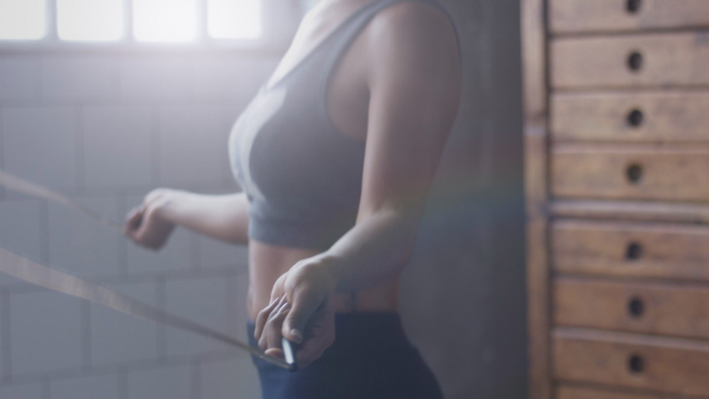 african american woman makes a jump rope routine in sunny loft for healthy life side view body closeup. Soft focusocus on hand