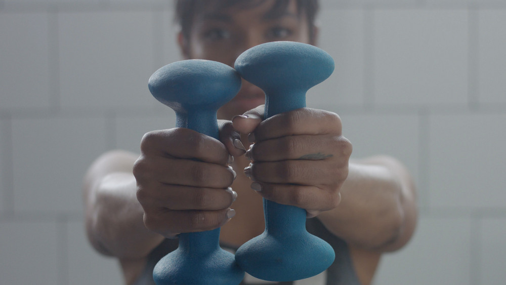 black woman portrait during weight training closeup with foucus on hand with weight moving to a camera