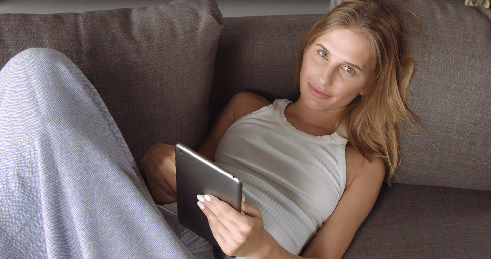 Camera starts with a pretty girl on the couch reading something on her tablet and goes off to industrial grey floor