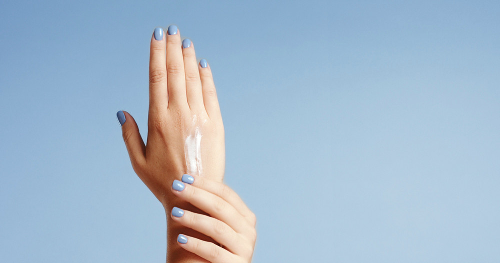 Clean well manicured hands of a young woman, applying hand cream, skin care on light blue background