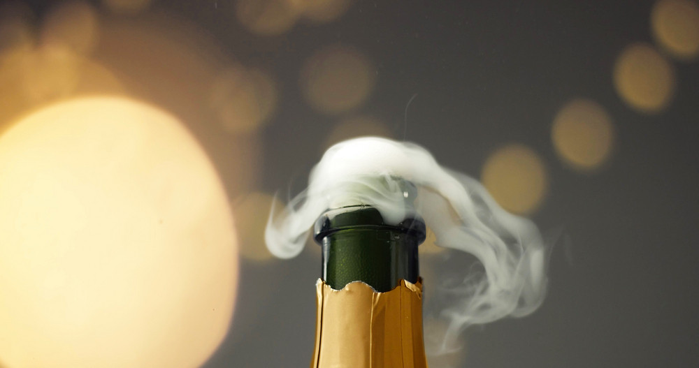 Close up slowmotion of man\'s hands opening a bottle of champagne on gray background with lights and flares