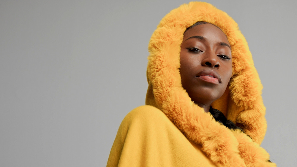 closeup portrait of black woman wears yellow hood with faux fur watching to the camera