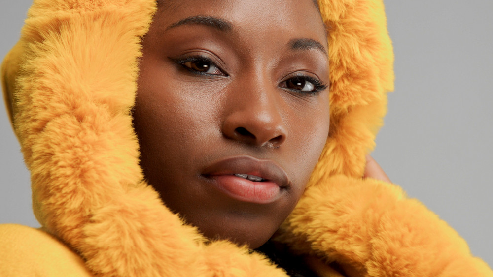 closeup portrait of black woman wears yellow hood with faux fur
