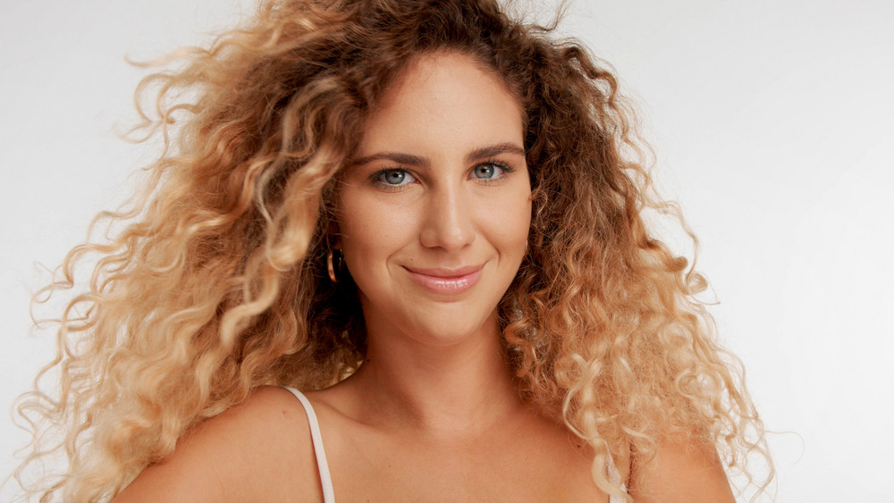 closeup portrait of model with big curly blonde hair blowing and she is smiling slightly