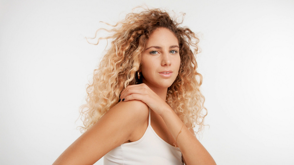 head and shoulders plan of model with big curly blonde hair in studio and blowing hair with serious face watching to the camera