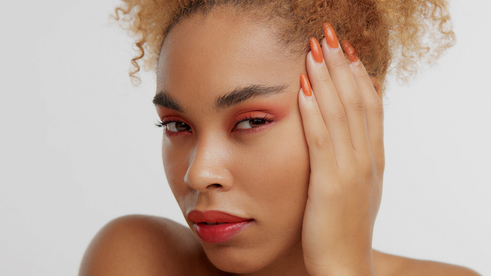 mixed race black blonde model with curly hair with bright red makeup with turned to the left face watching to the camera