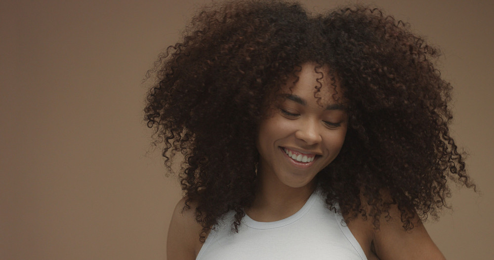 mixed race black woman portrait with big afro hair, curly hair in beige background. Natural laughing