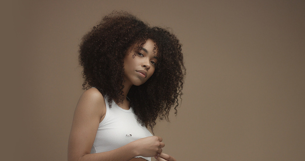 mixed race black woman portrait with big afro hair, curly hair in beige background