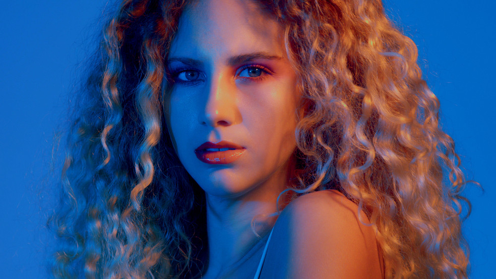 serious gorgeous woman with huge curly blond hair. Coloured light portrait