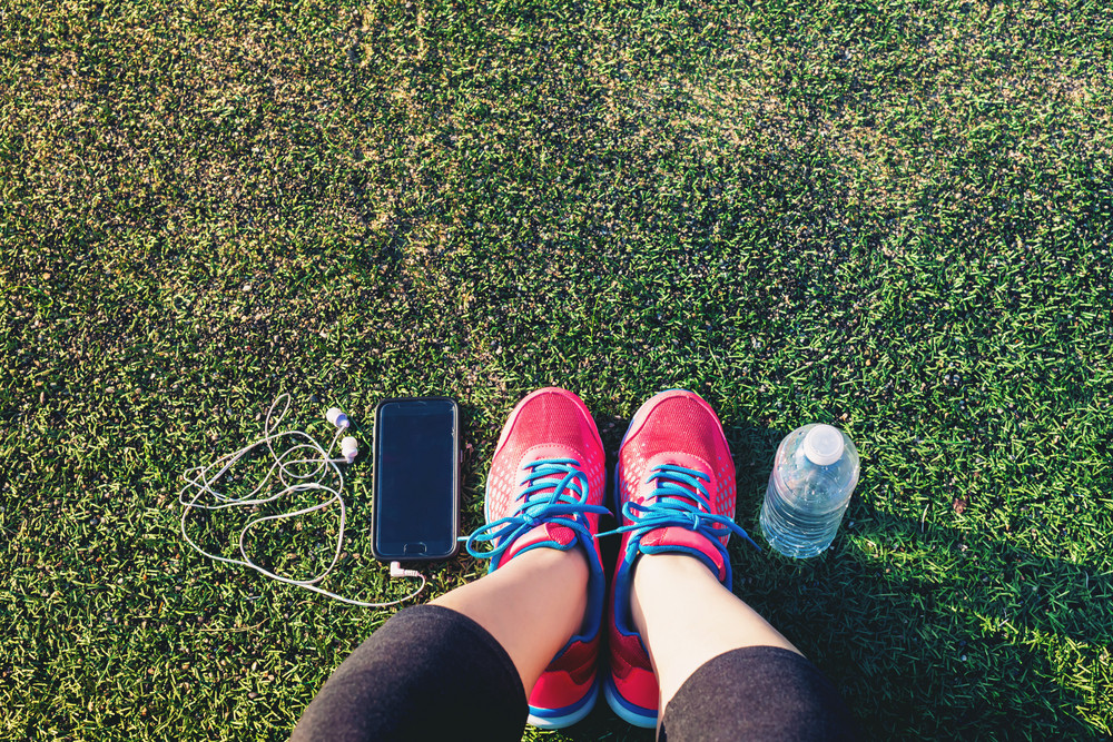 Female runner looking down at her feet, phone and water bottle in a field