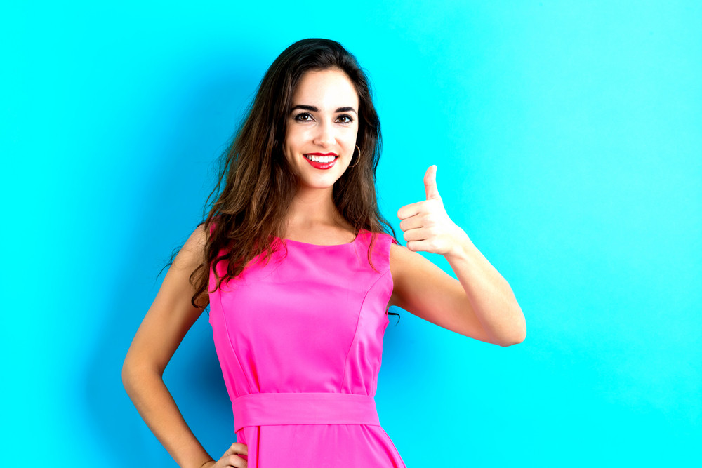 Happy young woman giving a thumb up on a blue background