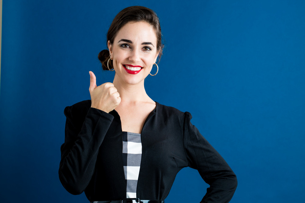 Happy young woman giving a thumb up on a dark blue background