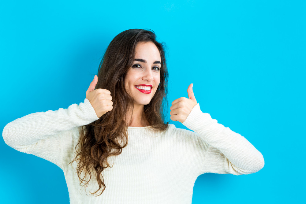 Happy young woman giving thumbs up on a blue background