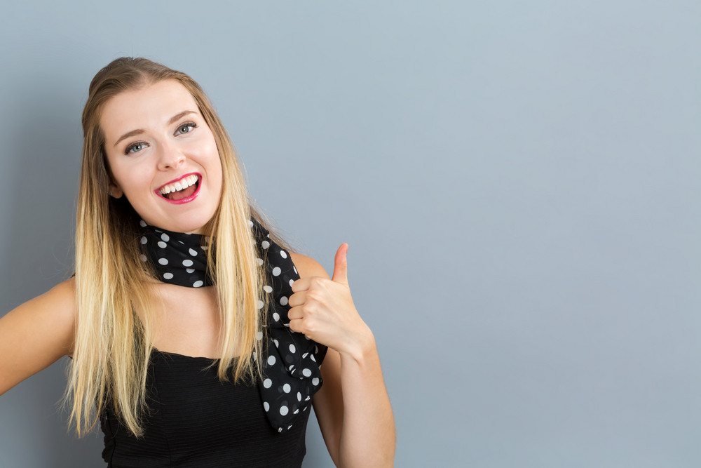 Happy young woman giving thumbs up on gray background