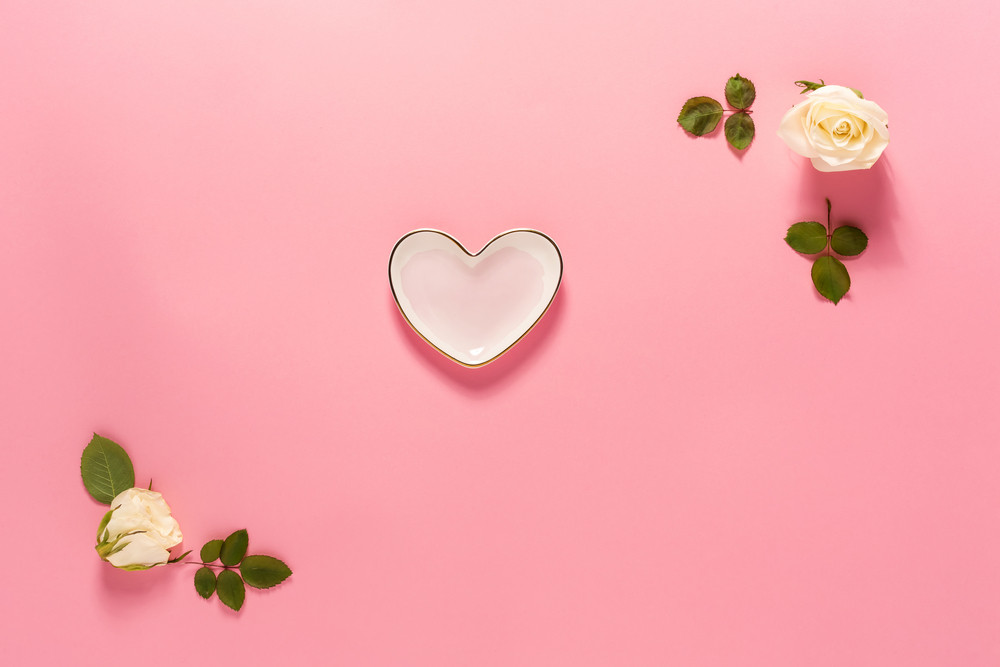 Heart-shaped dish with white rose frame on a pink background
