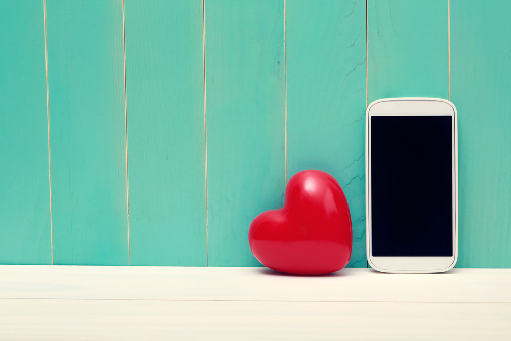 Love and technology theme with big red heart and smart phone