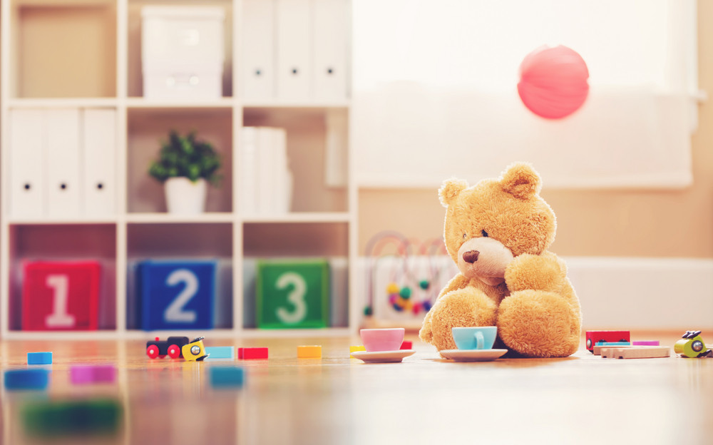 Teddy bear inside a child\'s play room surrounded by toys