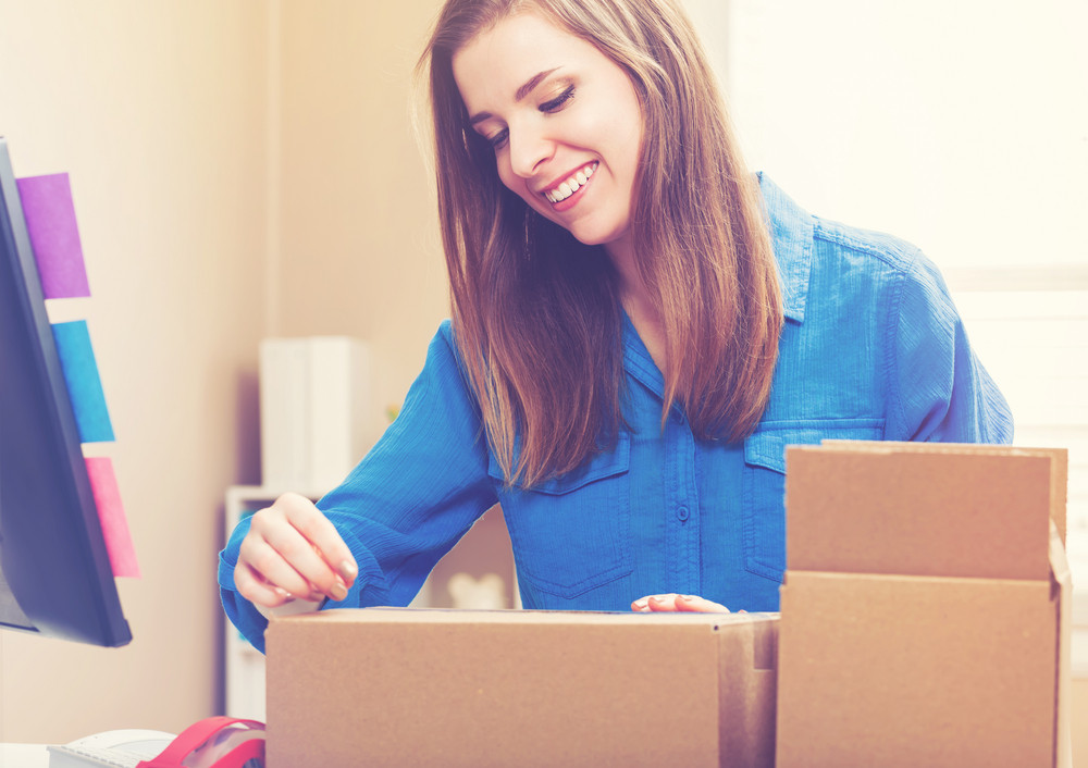 Young woman taping boxes to be shipped in her home office