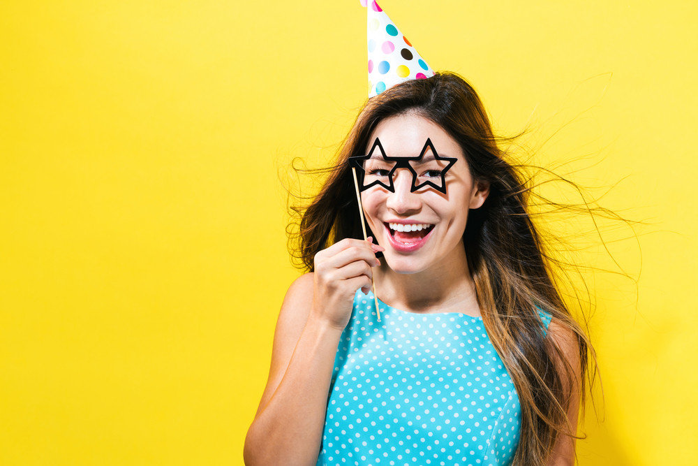Young woman with party hat with paper party sticks on a yellow background