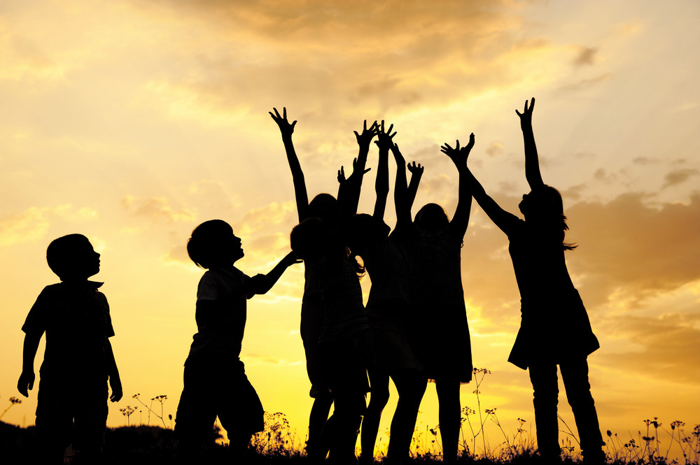 Group of children silhouettes playing on nature field at sunset ...