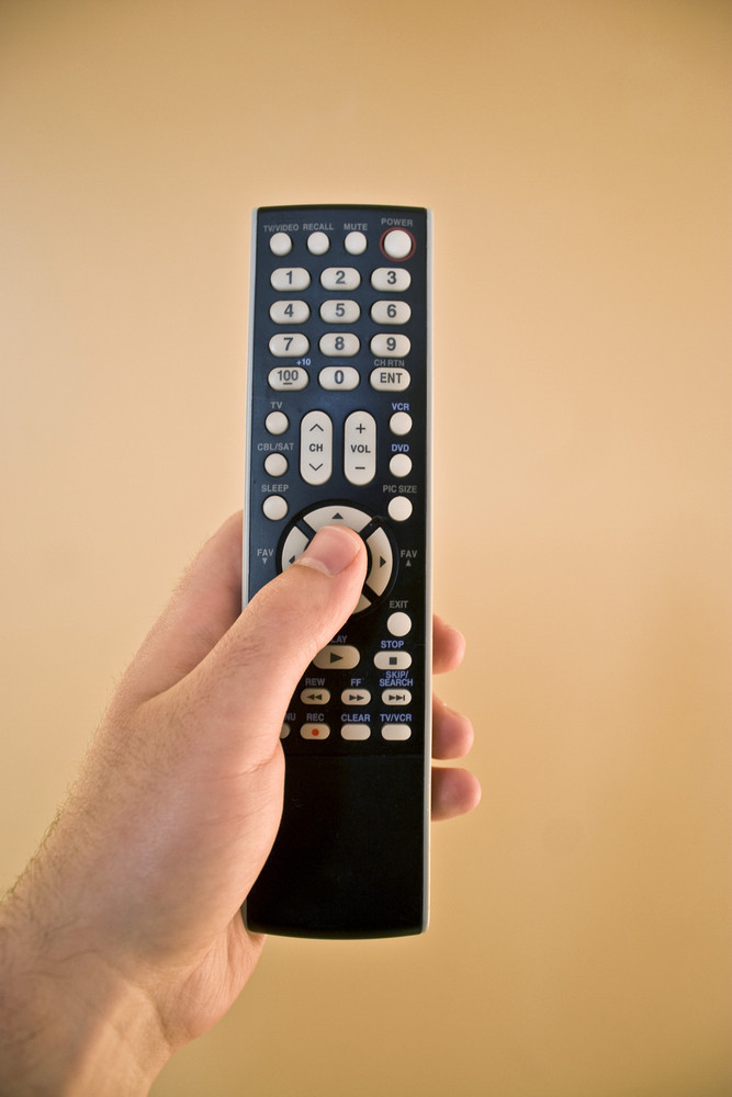 A hand holding a remote control isolated over a gold background.