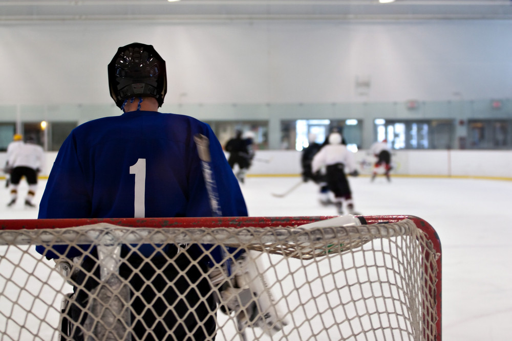 A hockey goalie awaiting the return of the puck so he can resume his defensive role. Shallow depth of field.