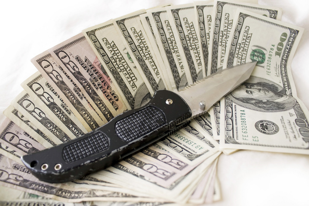 A knife and some fanned out cash laying on a bed. This works for all sorts of illegal activities such as prostitution, drug dealing, and gang activity.