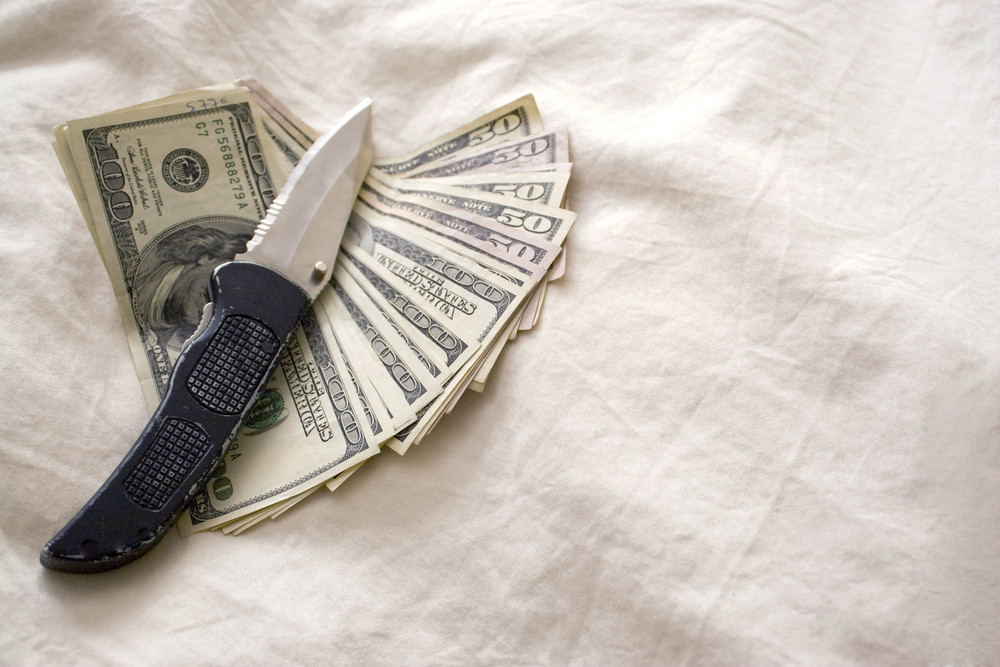 A knife and some fanned out cash laying on a bed.