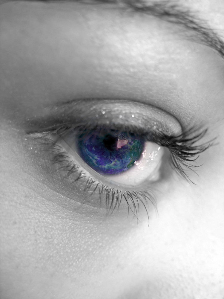 A macro shot of a pretty woman\'s eye with selective color. An image of the earth is superimposed inside the eye.