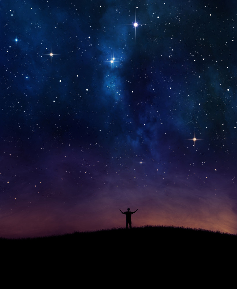 A man lifting his hands in praise under night sky.