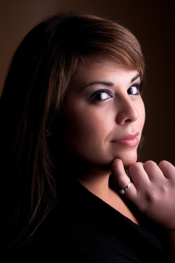 A pretty young Hispanic female posing with her hand on her chin thinks deeply about something on her mind.