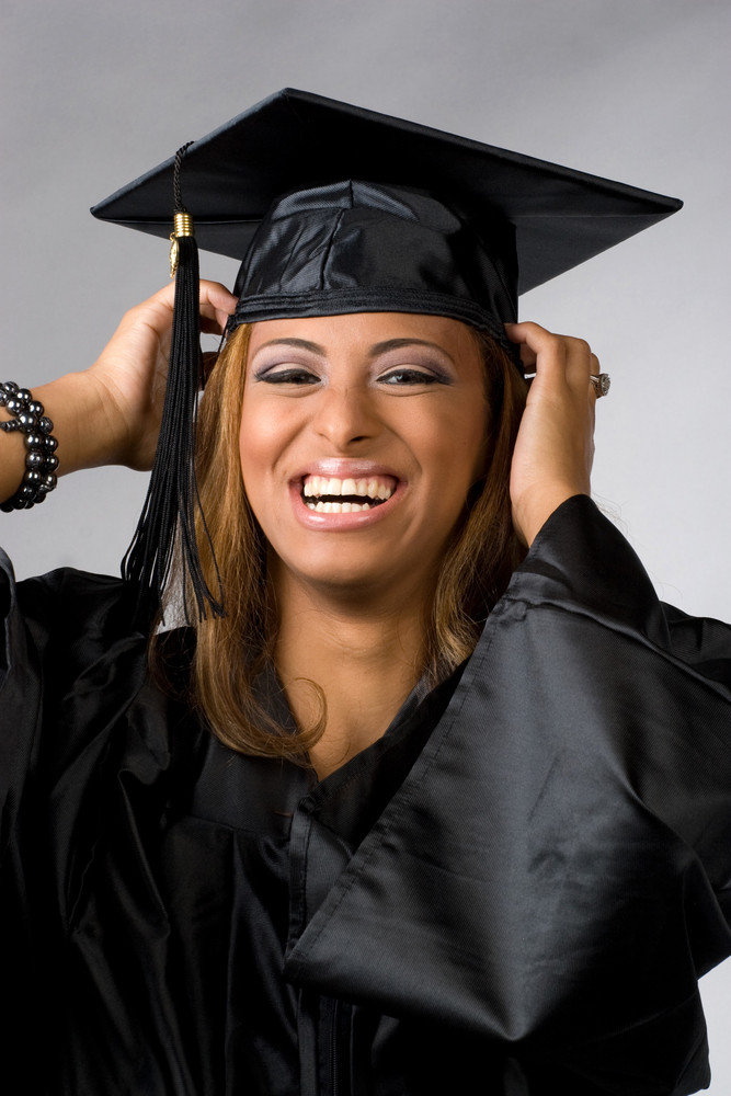 A recent graduate posing in her cap and gown isolated over a silver background.