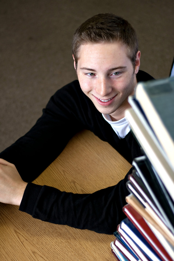 A student happily looks up at the high pile of textbooks he has to go through to do his homework assignment.