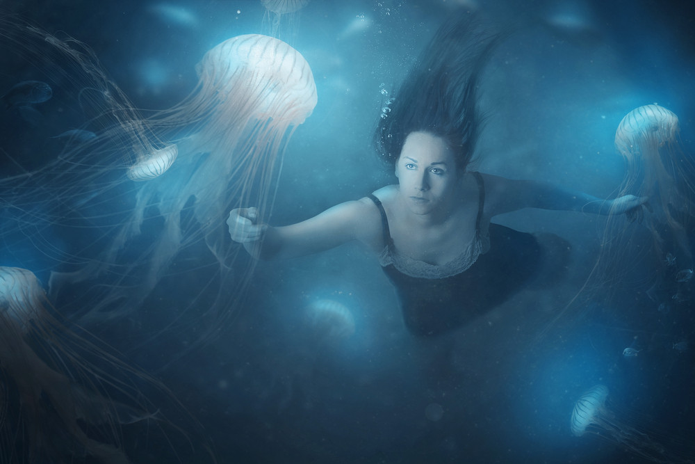 A woman swimming in the deep ocean with jelly fish