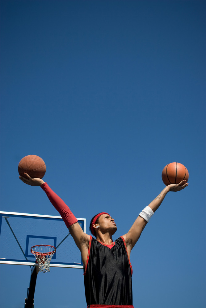 A young basketball player holding up two basketballs in the shape of a V.