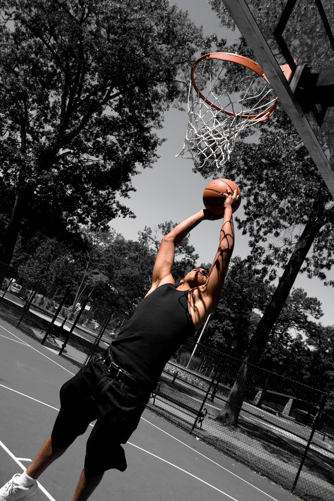 A young man driving to the basketball hoop for a dunk with selective color.