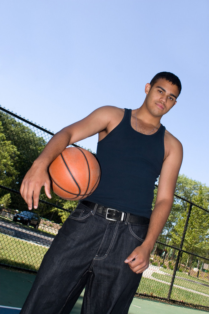 A young man posing at the basketball court with a ball.