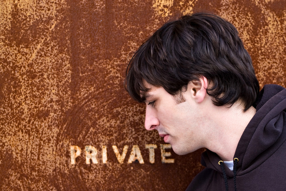 A young man standing outside an old door or entrance that reads PRIVATE. A great image for any identity theft concept.