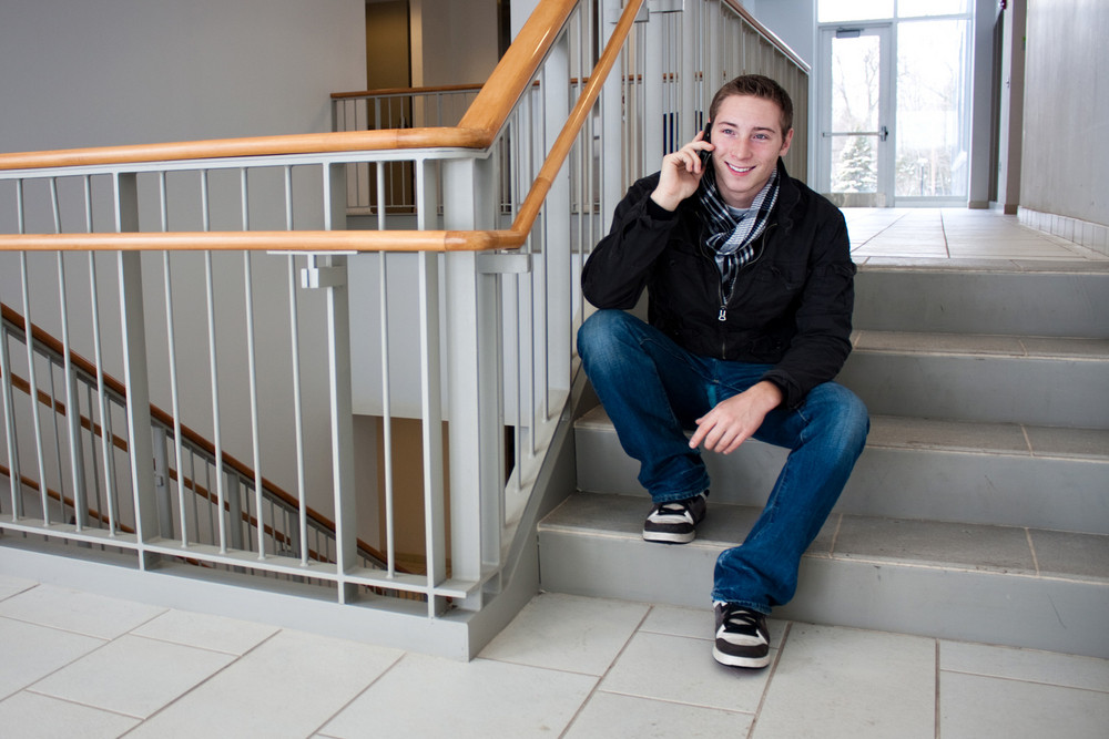 A young man stops to sit on the stairs and talk on his cell phone.